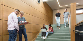 Gruppe auf der Treppe Zwei Studierende laufen eine Treppe herunter, zwei sitzen auf der Treppe und zwei stehen davor.